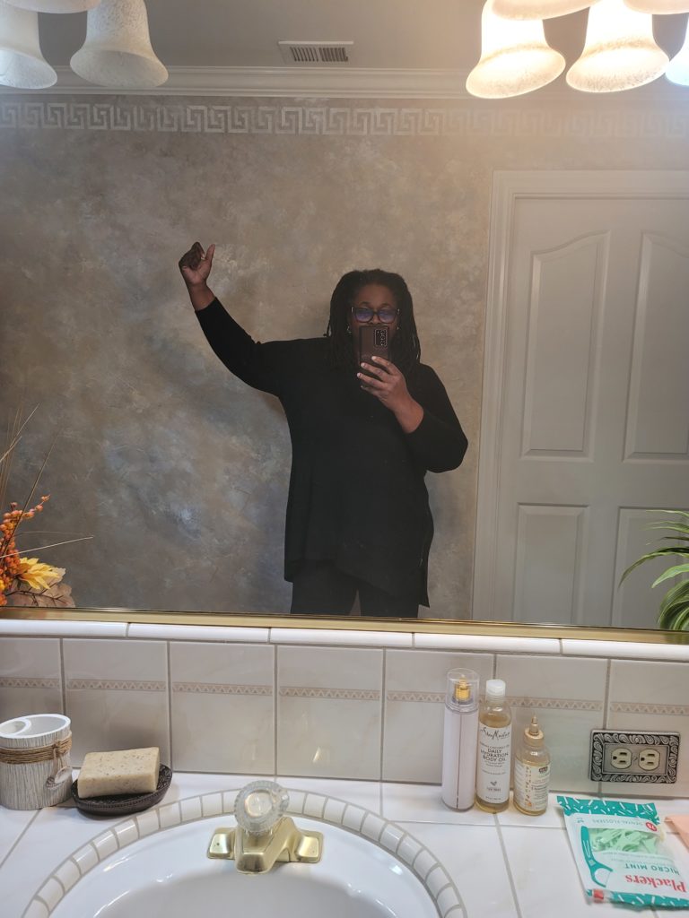 Woman (myself) facing mirror with right  arm lifted in the air in a power pose, This showing my week 2 size, as I move along my fitness journey