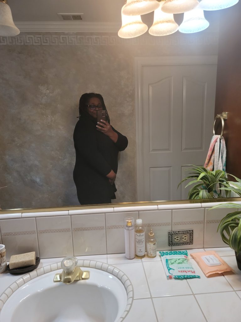 Side profile of woman (myself) wearing a black sweater and black pants showing off size in week 2 of fitness journey