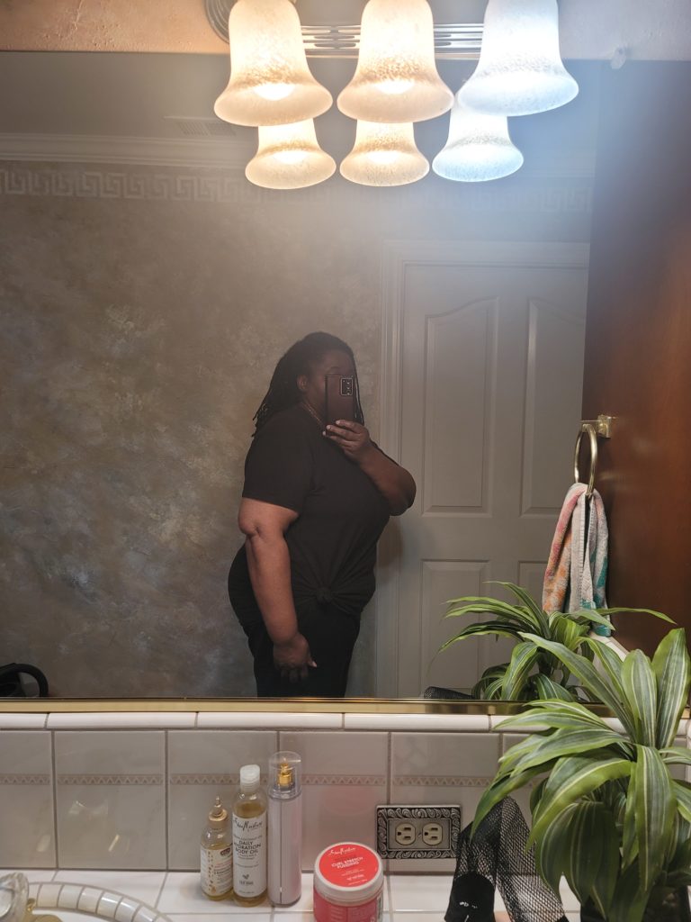 The fitness journey of a woman posing in front of mirror showing her side profile view. This is also to show size at the beginning of the fitness process.